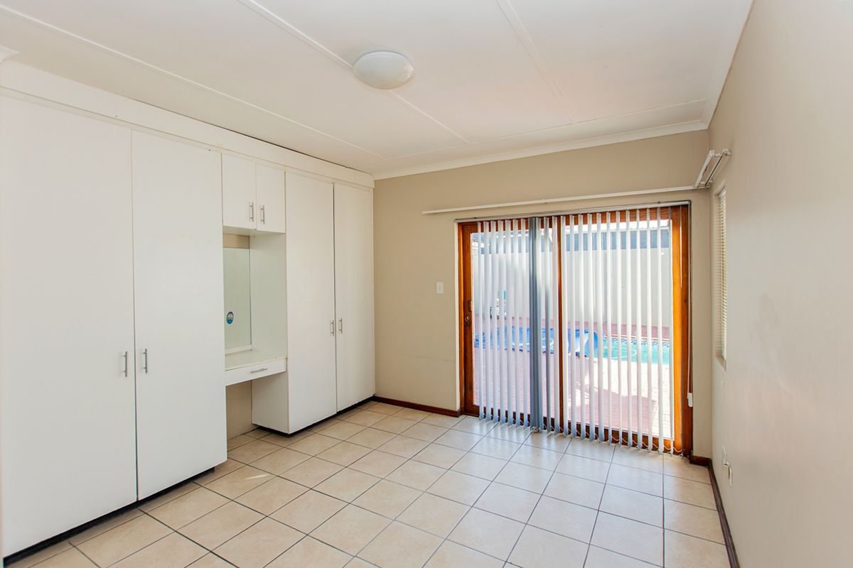 A bright bedroom featuring built-in cupboards with an integrated vanity, tiled flooring, and a sliding glass door providing access to the pool area.
