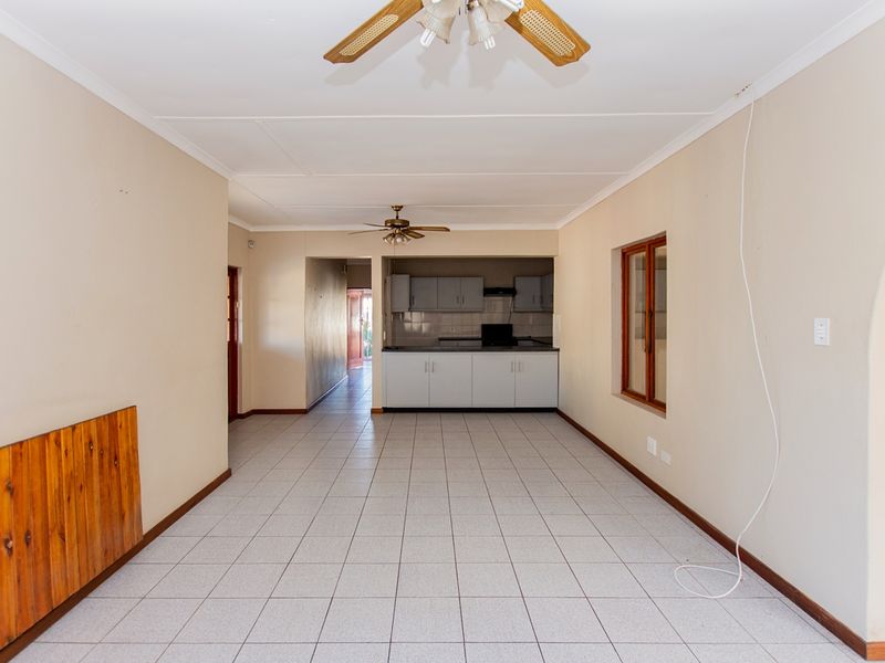 An open-plan living and kitchen area featuring tiled flooring, ceiling fans, and basic cabinetry, presenting a blank canvas for renovation.