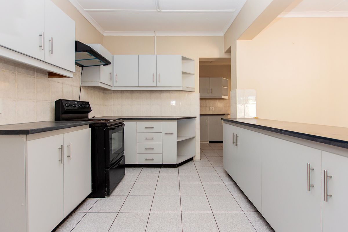 A clean, functional kitchen featuring white cabinetry, dark laminate countertops, tiled flooring, and a tiled backsplash, with an adjacent scullery area visible.