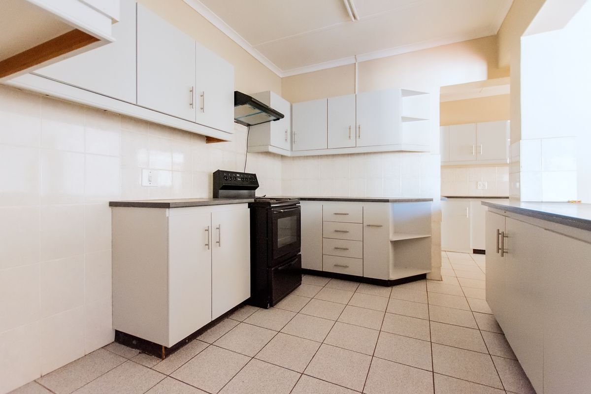 A functional, empty kitchen featuring white cabinetry, tiled flooring, tiled splashbacks, and a black freestanding oven with an extractor fan.