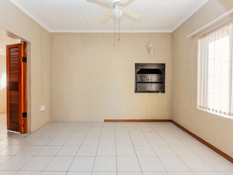An empty living room featuring tiled flooring, a ceiling fan, and a built-in fireplace, offering a blank canvas for renovation.