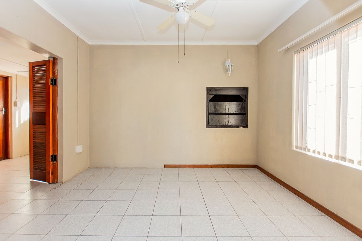 An empty living room featuring tiled flooring, a ceiling fan, and a built-in fireplace, offering a blank canvas for renovation.