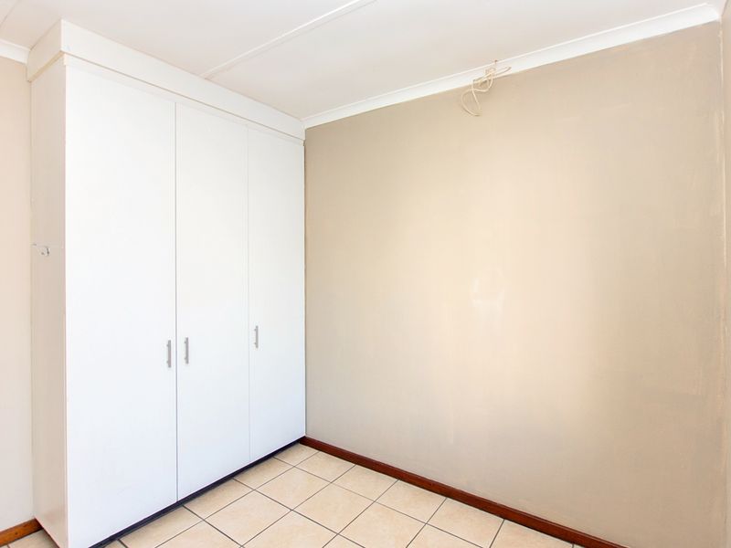 A clean, empty bedroom featuring neutral wall tones, tiled flooring, and built-in white cupboards, ready for personalization.