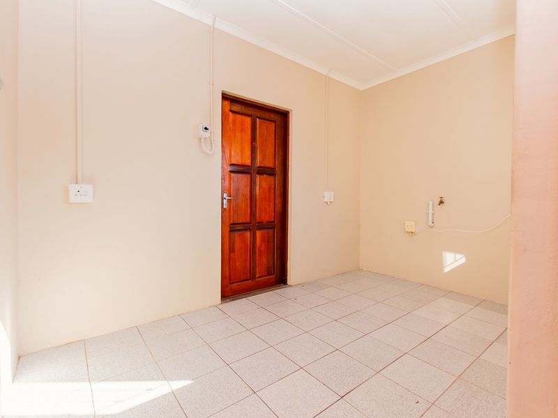 A clean, empty laundry room featuring tiled flooring, plumbing connections for appliances, and a solid timber door.