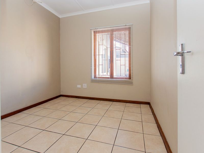 An empty bedroom featuring neutral wall paint, tiled flooring, and a window fitted with venetian blinds.