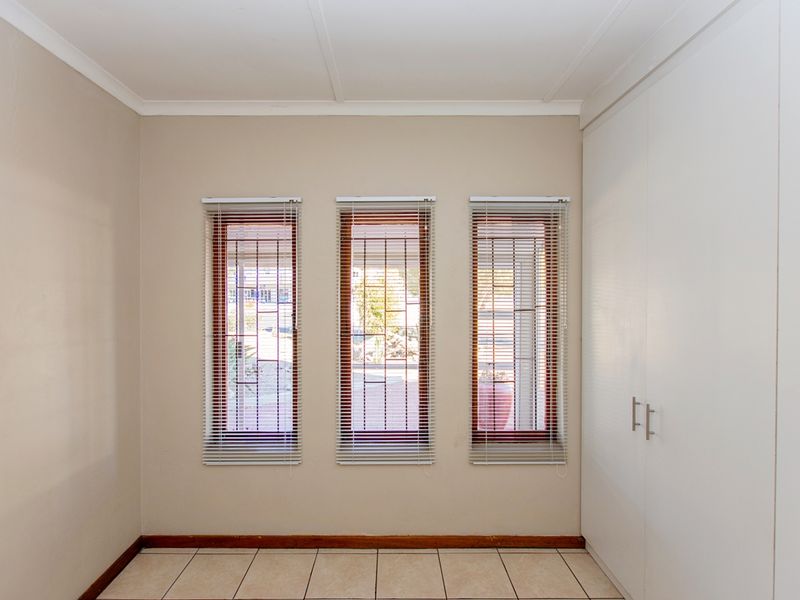 An empty bedroom featuring neutral walls, tiled flooring, built-in cupboards, and three windows fitted with security bars and venetian blinds.