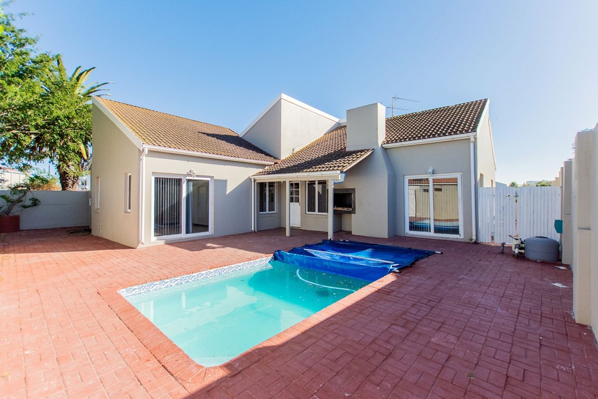 Rear exterior view featuring a paved patio area, a swimming pool with a cover, and a built-in braai facility.
