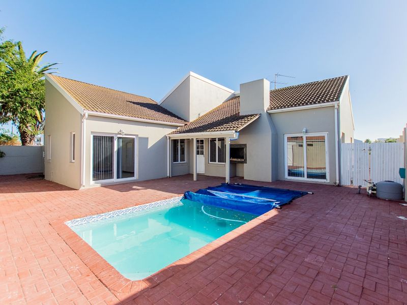 Rear exterior view featuring a paved patio area, a swimming pool with a cover, and a built-in braai facility.