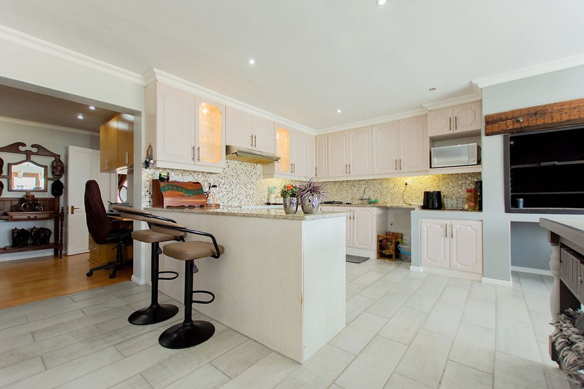 A well-maintained kitchen featuring light-toned cabinetry, granite countertops, a mosaic tile backsplash, and a functional breakfast bar with integrated lighting.