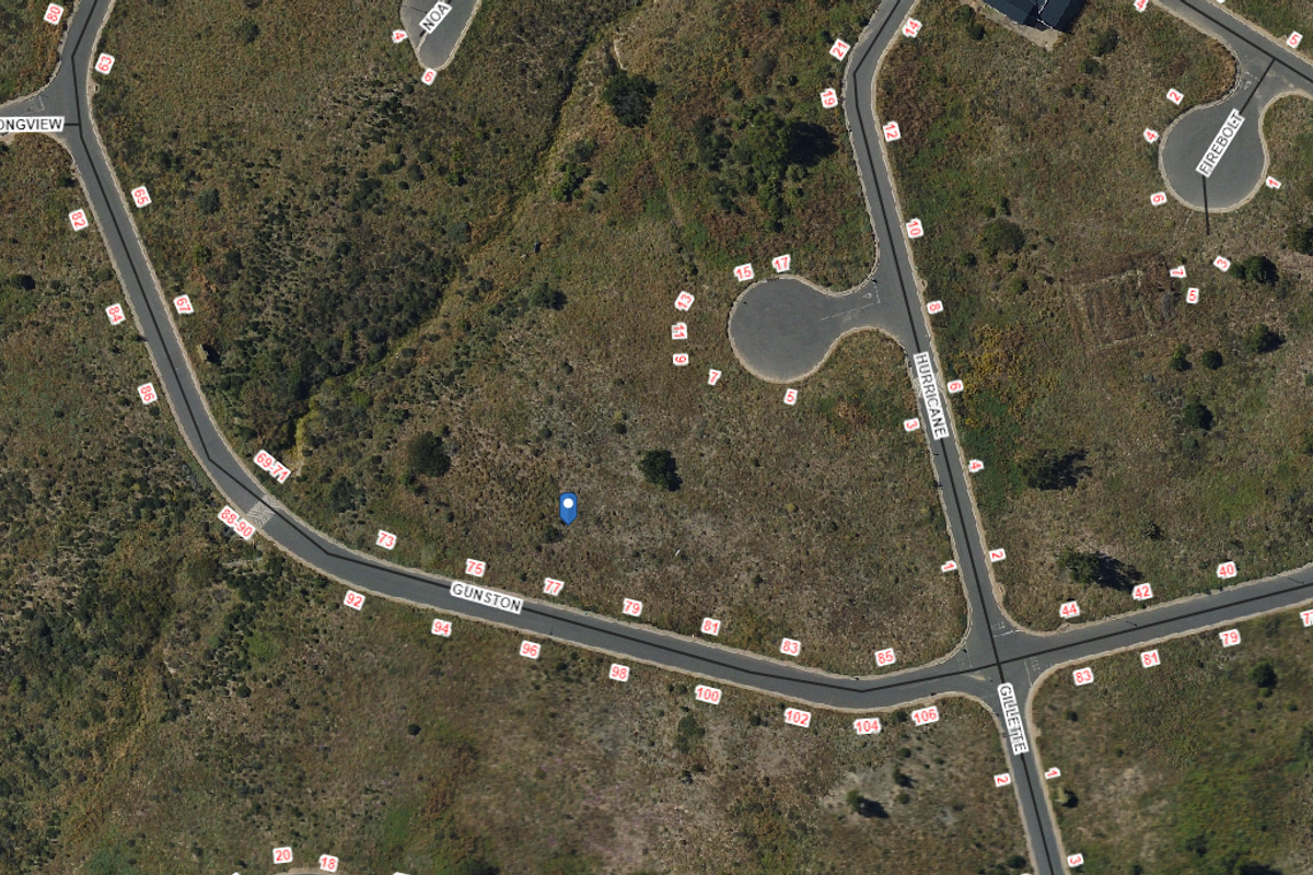An aerial view of a vacant residential plot situated within a developed estate, showing surrounding roads and property boundaries.