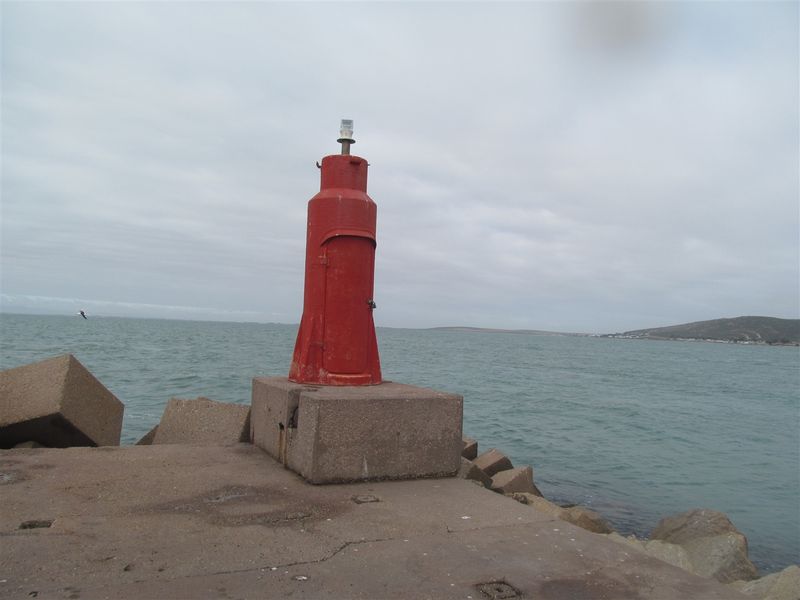 A red navigation beacon situated on a concrete pier overlooking the ocean.