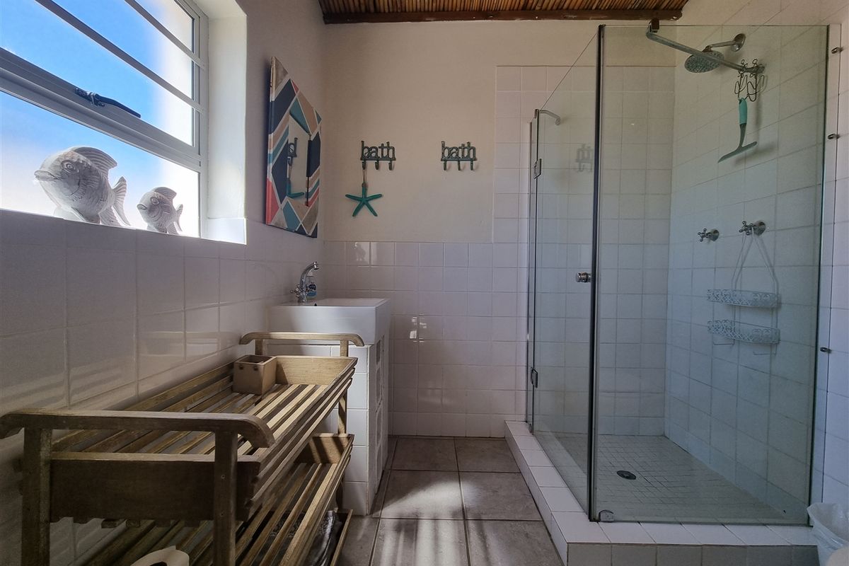 A functional bathroom featuring a glass-enclosed shower, tiled walls and flooring, a basin, and exposed timber ceiling beams.