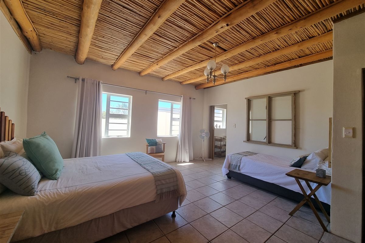 Spacious bedroom featuring a unique exposed timber beam and reed ceiling, tiled flooring, and natural light through multiple casement windows.