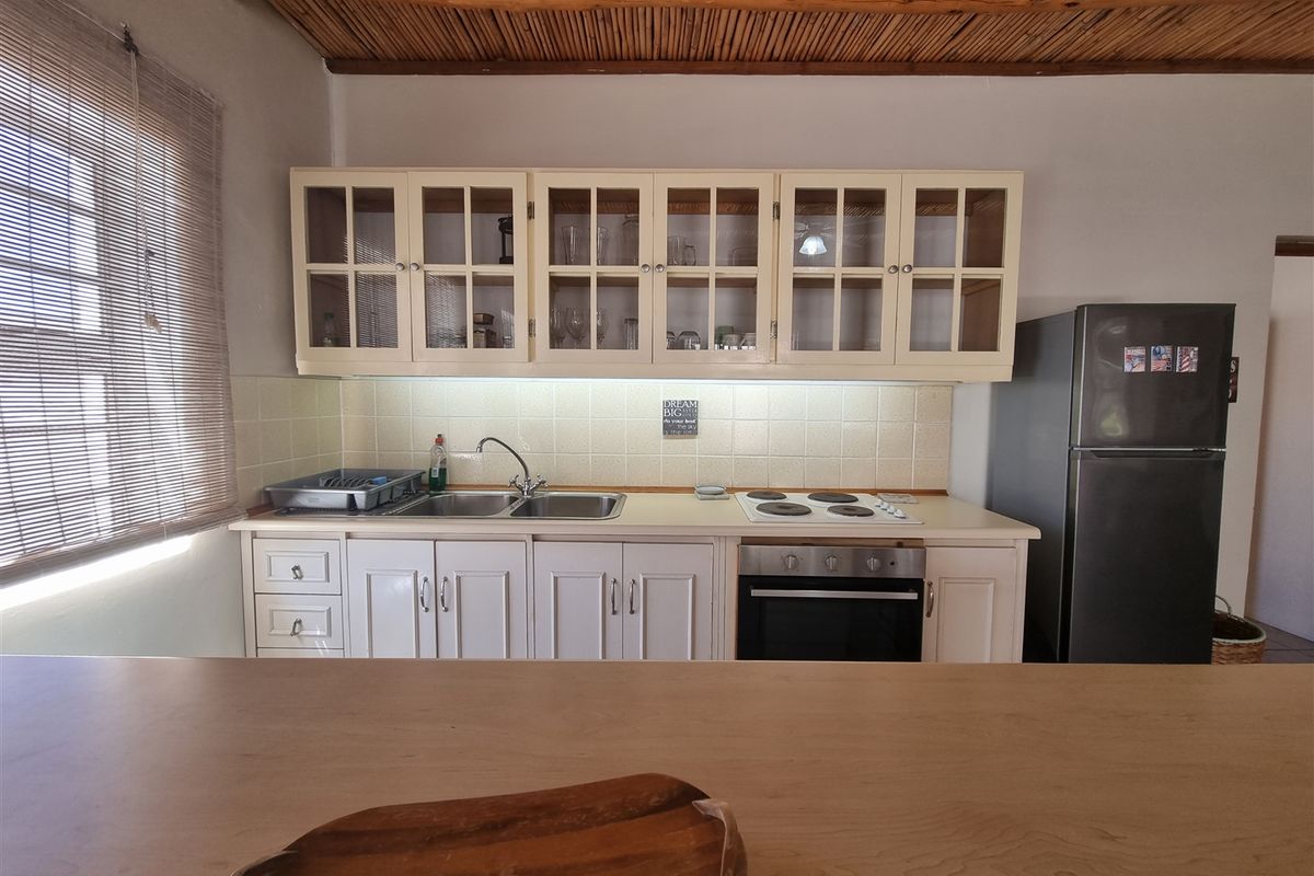 A functional kitchen featuring cream cabinetry, a tiled backsplash, built-in oven and hob, and a rustic timber beam ceiling.