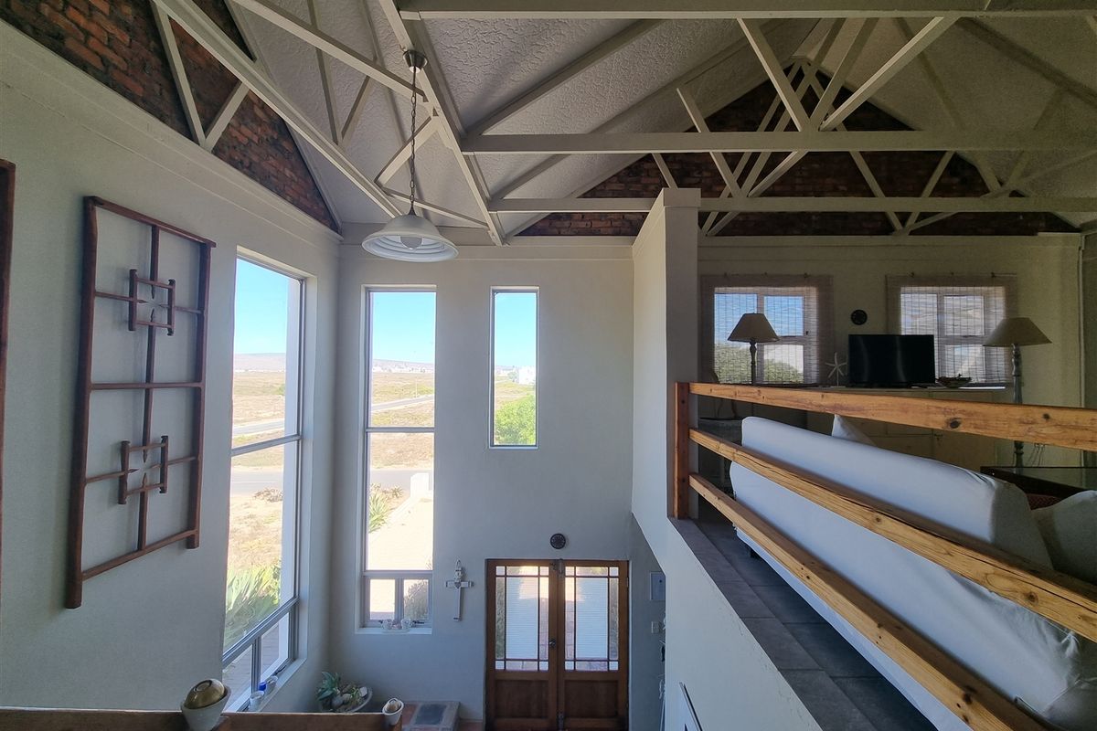 Spacious living area featuring a double-volume vaulted ceiling with exposed trusses, brick accents, and a mezzanine level overlooking the entrance.