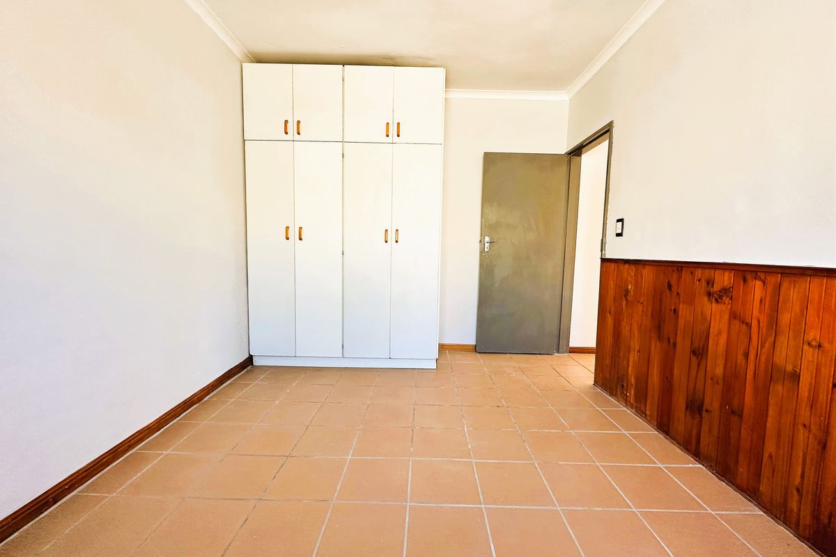 A vacant bedroom featuring tiled flooring, built-in cupboards, and decorative timber wall paneling, offering a blank canvas for personalization.