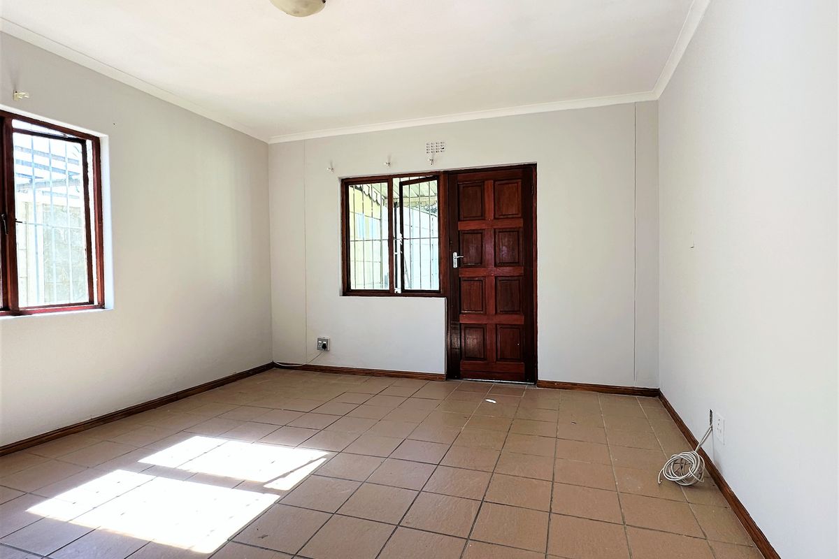 An empty living room featuring tiled flooring, a timber door, and security bars on the windows, offering a blank canvas for interior design.