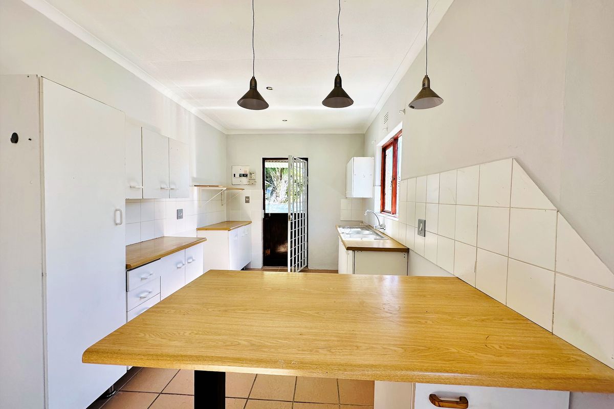 A functional kitchen featuring white cabinetry, wood-look laminate countertops, tiled backsplash, and direct access to the rear exterior.
