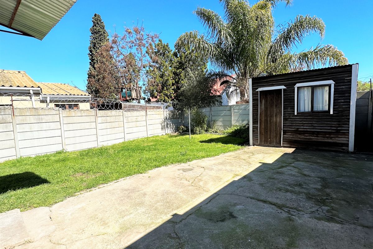 Rear garden area featuring a concrete paved patio, lawn, and a detached timber storage shed enclosed by a precast concrete boundary wall.