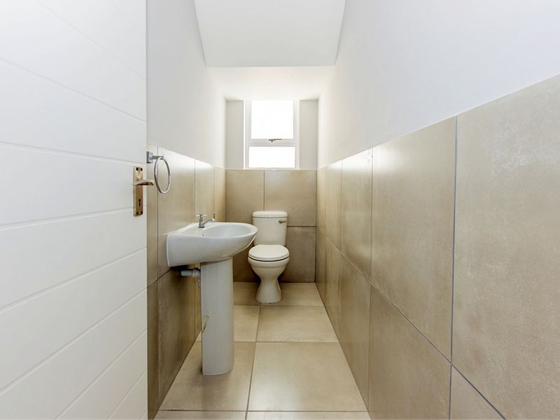 A compact guest bathroom featuring neutral floor-to-ceiling wall tiles, a pedestal basin, and a standard toilet.