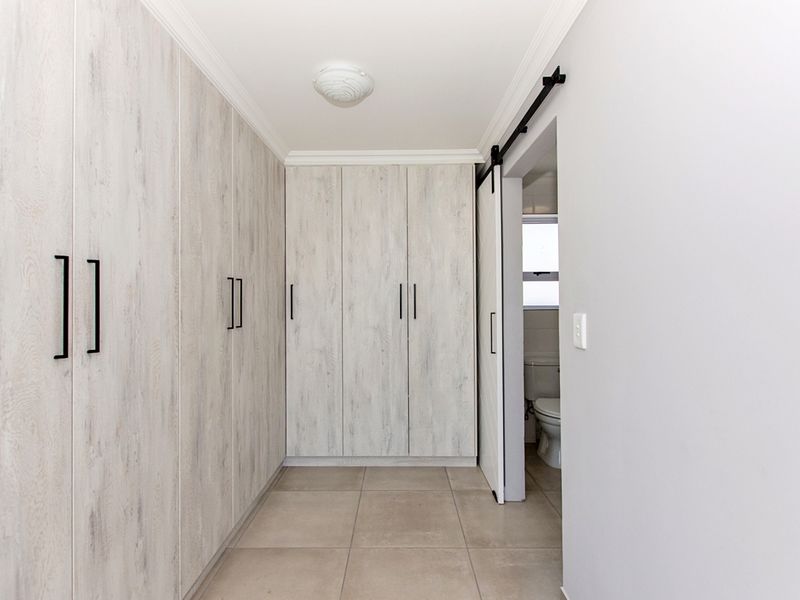 A clean, modern hallway featuring extensive built-in cupboards with light wood-grain finish, tiled flooring, and a sliding barn door leading to an adjacent bathroom.