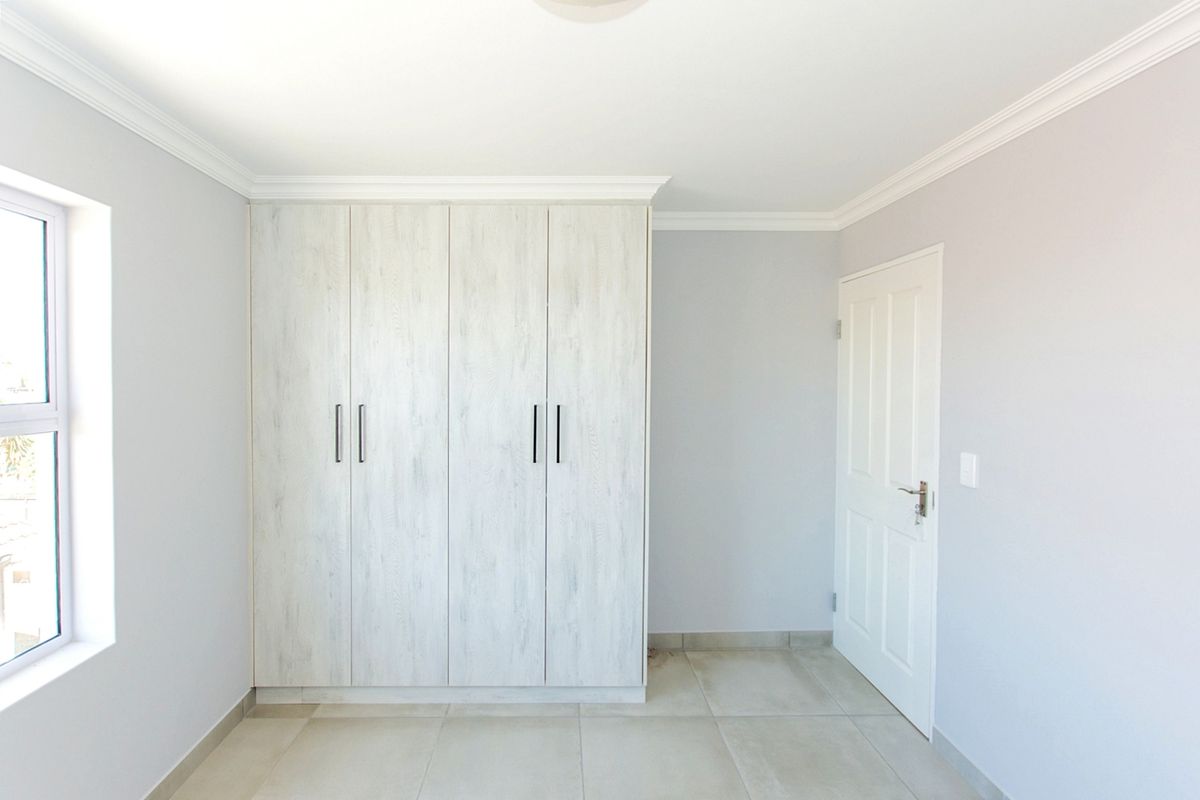 A bright, empty bedroom featuring neutral tiled flooring, a modern built-in wardrobe with light wood-grain finish, and classic ceiling cornicing.