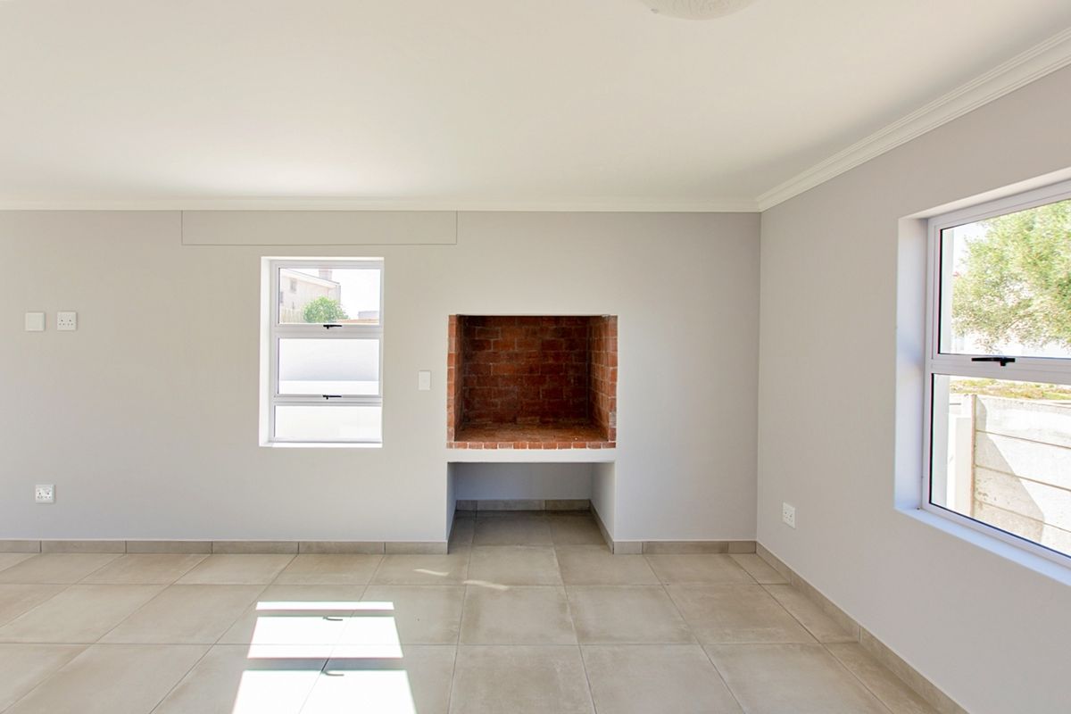 A bright, empty living room featuring neutral tiled flooring, aluminium windows, and a built-in brick fireplace, offering a clean canvas for interior design.