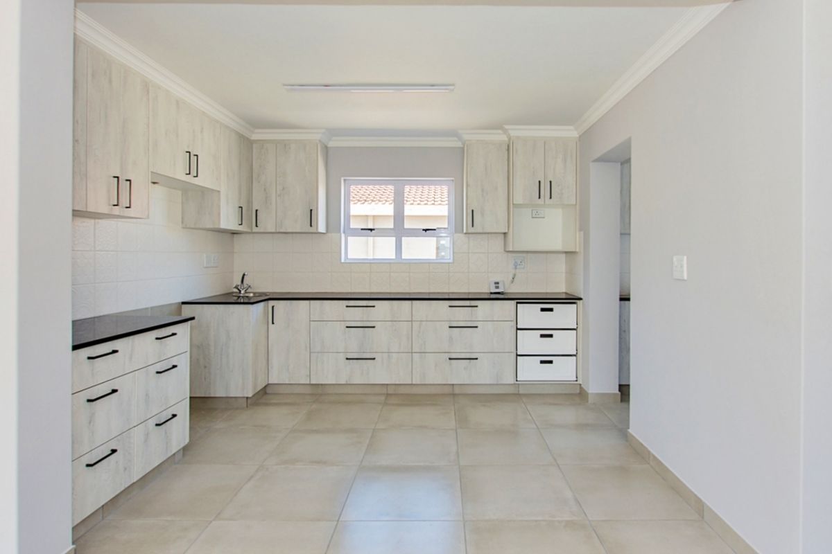 A clean, modern kitchen featuring light wood-grain cabinetry, dark countertops, tiled flooring, and a functional layout with ample storage space.