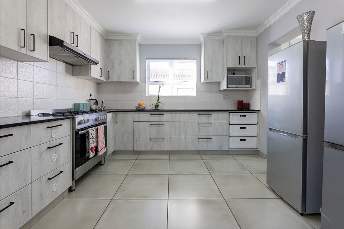 A well-maintained kitchen featuring light wood-grain cabinetry, tiled flooring, a gas stove with extractor fan, and a built-in microwave.