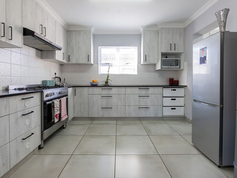 A well-maintained kitchen featuring light wood-grain cabinetry, tiled flooring, a gas stove with extractor fan, and a built-in microwave.