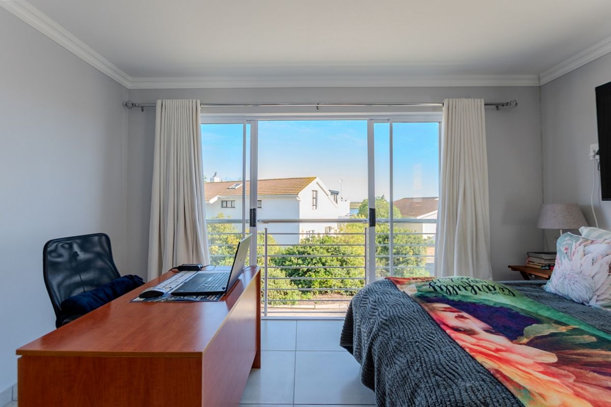 A well-maintained bedroom featuring tiled flooring, crown molding, and a large sliding glass door that opens onto a balcony with neighborhood views.