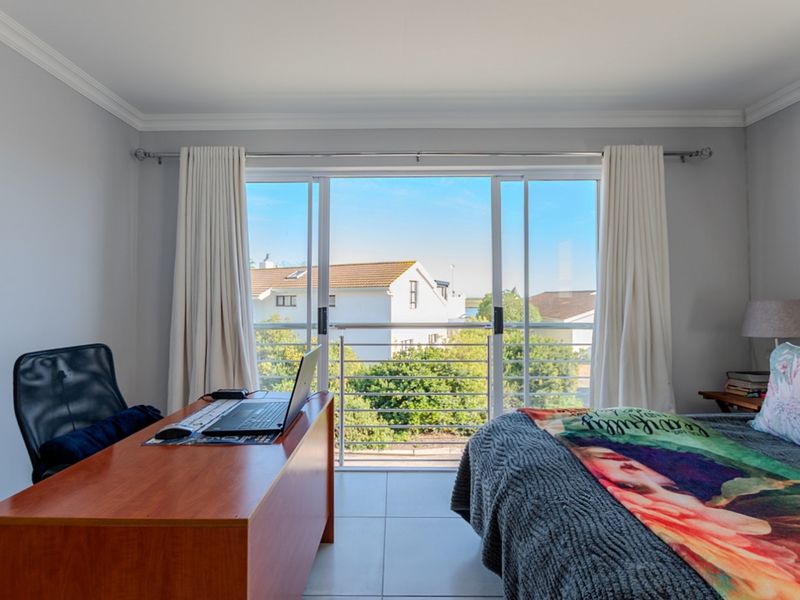 A well-maintained bedroom featuring tiled flooring, crown molding, and a large sliding glass door that opens onto a balcony with neighborhood views.