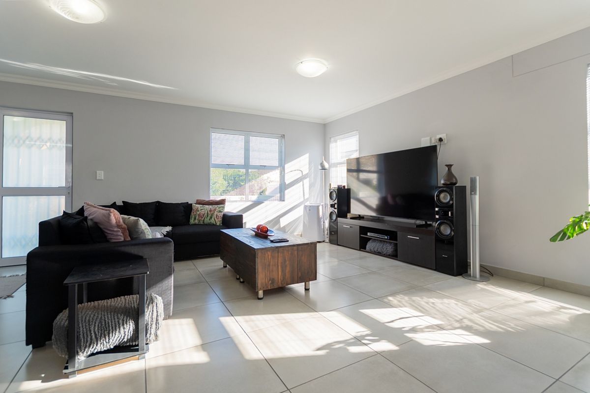 A bright and spacious living room featuring neutral tiled flooring, large windows allowing natural light, and clean wall finishes.