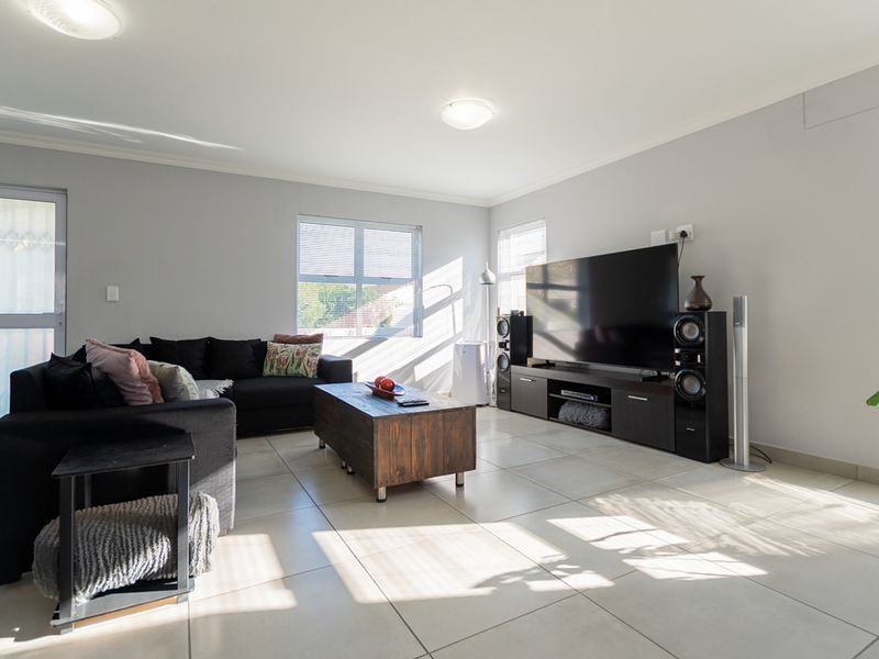 A bright and spacious living room featuring neutral tiled flooring, large windows allowing natural light, and clean wall finishes.
