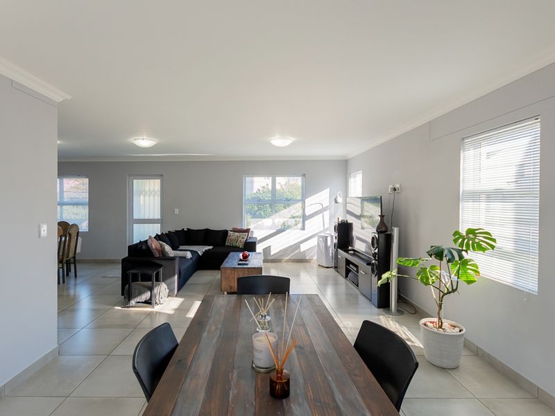Spacious open-plan living and dining area featuring neutral wall tones, large format floor tiles, and abundant natural light through multiple windows.
