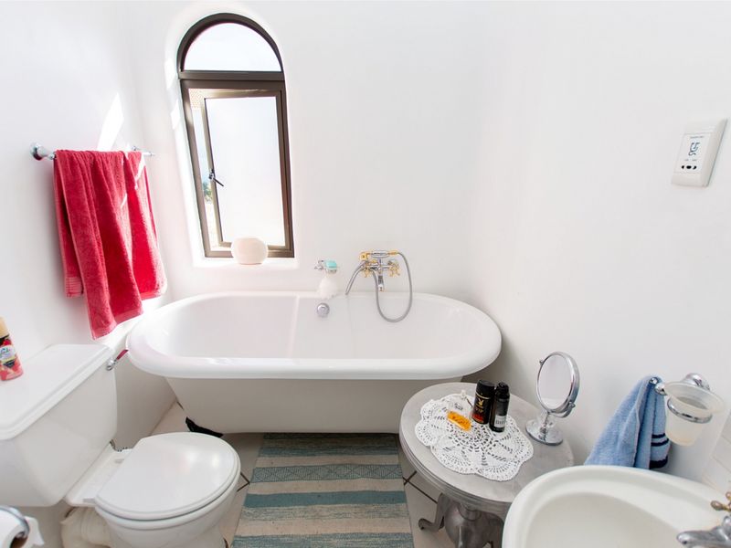 A bright bathroom featuring a classic freestanding bathtub, an arched window, a pedestal sink, and a standard toilet.