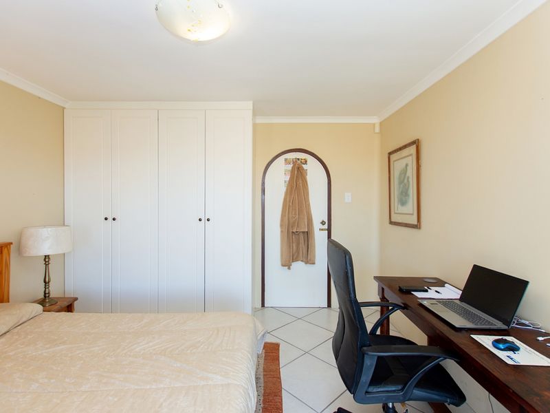 A functional bedroom featuring built-in white cupboards, tiled flooring, and an arched doorway, providing a practical layout for sleeping and workspace.