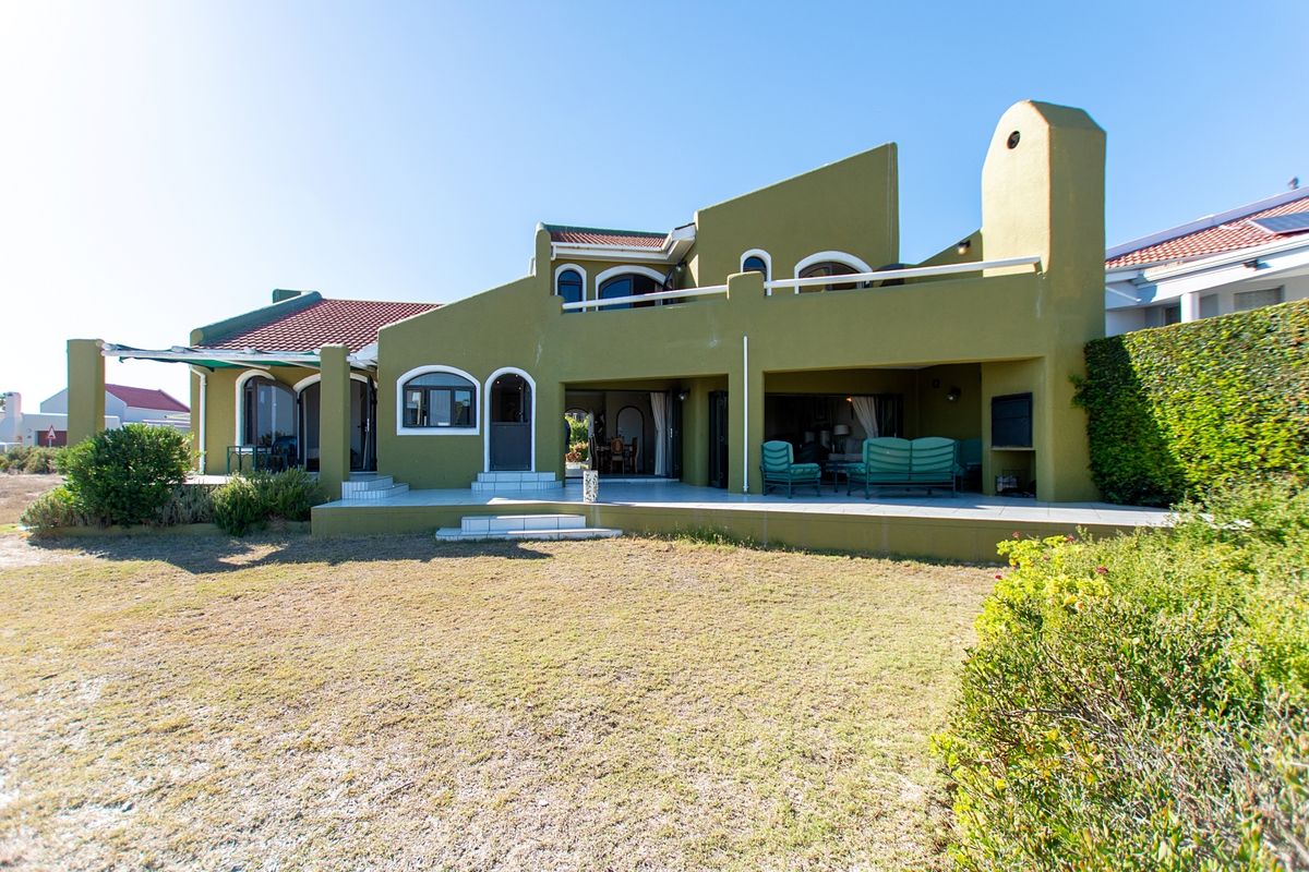 Rear view of a multi-level house featuring a covered patio with a built-in braai, upper balcony, and tiled roof architecture.
