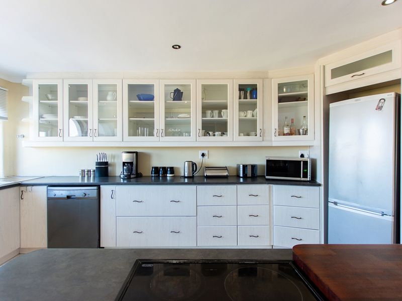 A well-maintained kitchen featuring light-toned cabinetry, glass-fronted display cupboards, dark countertops, and an integrated dishwasher with a built-in electric cooktop.
