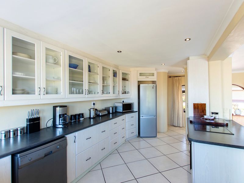 A well-lit kitchen featuring white cabinetry with glass-fronted uppers, dark countertops, tiled flooring, and integrated appliances, offering a clean and functional workspace.