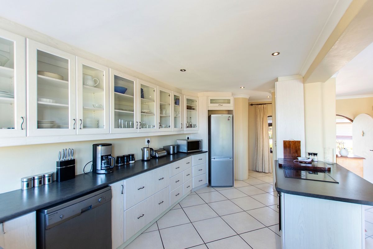 A well-lit kitchen featuring white cabinetry with glass-fronted uppers, dark countertops, tiled flooring, and integrated appliances, offering a clean and functional workspace.