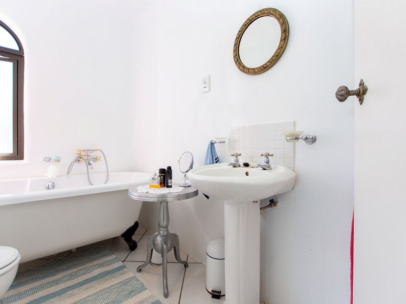 A bright bathroom featuring a classic clawfoot bathtub, a pedestal basin, and an arched window, offering a traditional aesthetic.