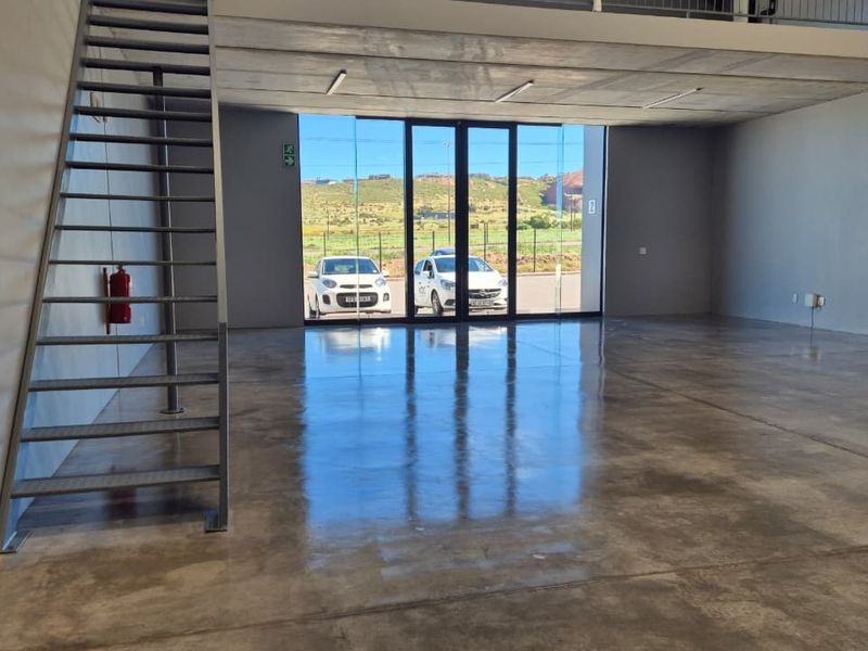 Spacious open-plan retail unit featuring polished concrete flooring, a modern metal staircase, and a mezzanine level with large glass frontage.