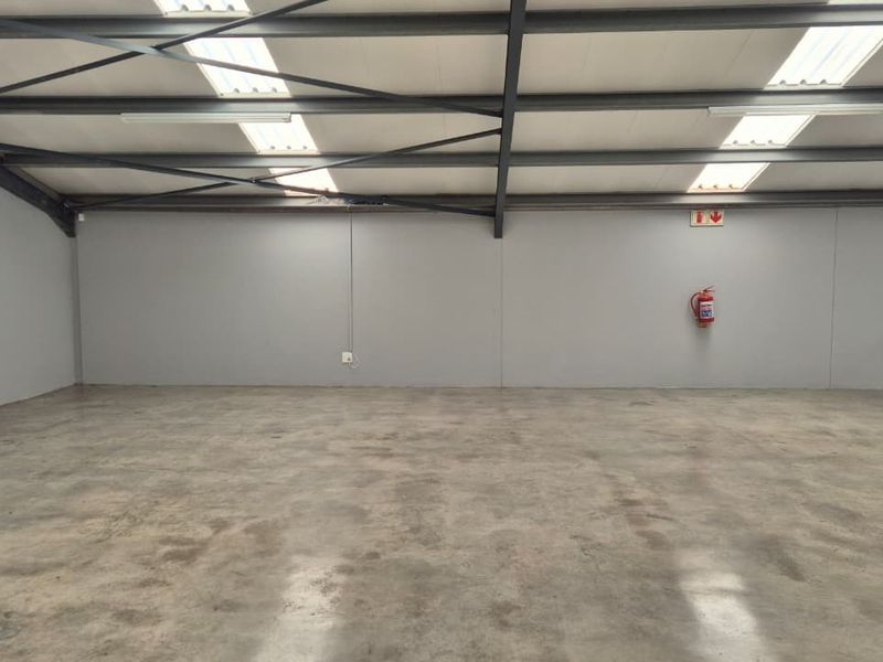 Spacious open-plan utility or warehouse area featuring polished concrete floors, exposed steel roof trusses, and natural light from integrated skylights.