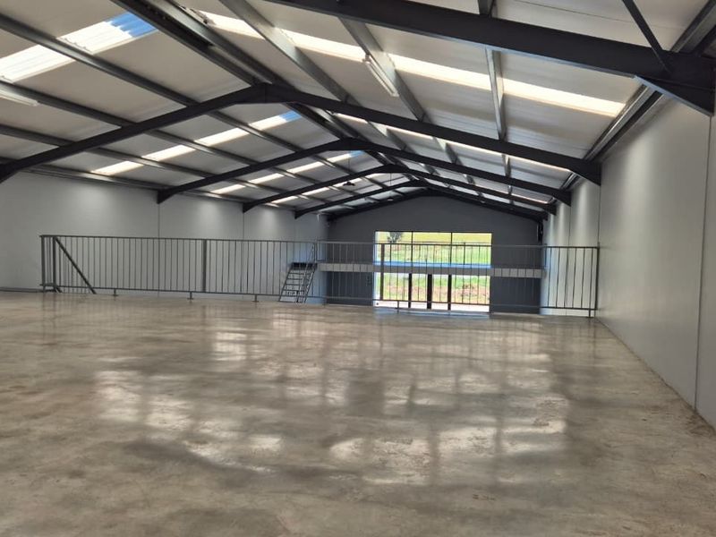 Spacious open-plan retail or industrial unit featuring polished concrete flooring, high ceilings with integrated skylights, and a mezzanine level with metal safety railings.
