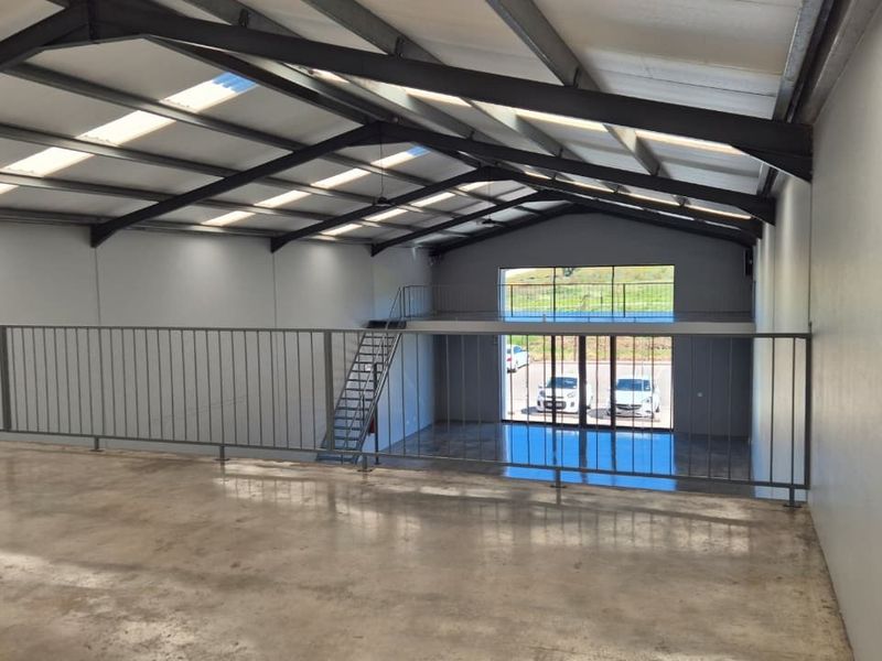 Spacious open-plan industrial unit featuring a mezzanine level, polished concrete floors, high ceilings with skylights, and large glass doors providing natural light.