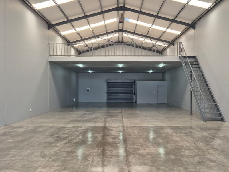 Spacious industrial warehouse unit featuring a concrete floor, mezzanine level with metal staircase, roller shutter door, and high-clearance roof with integrated skylights.