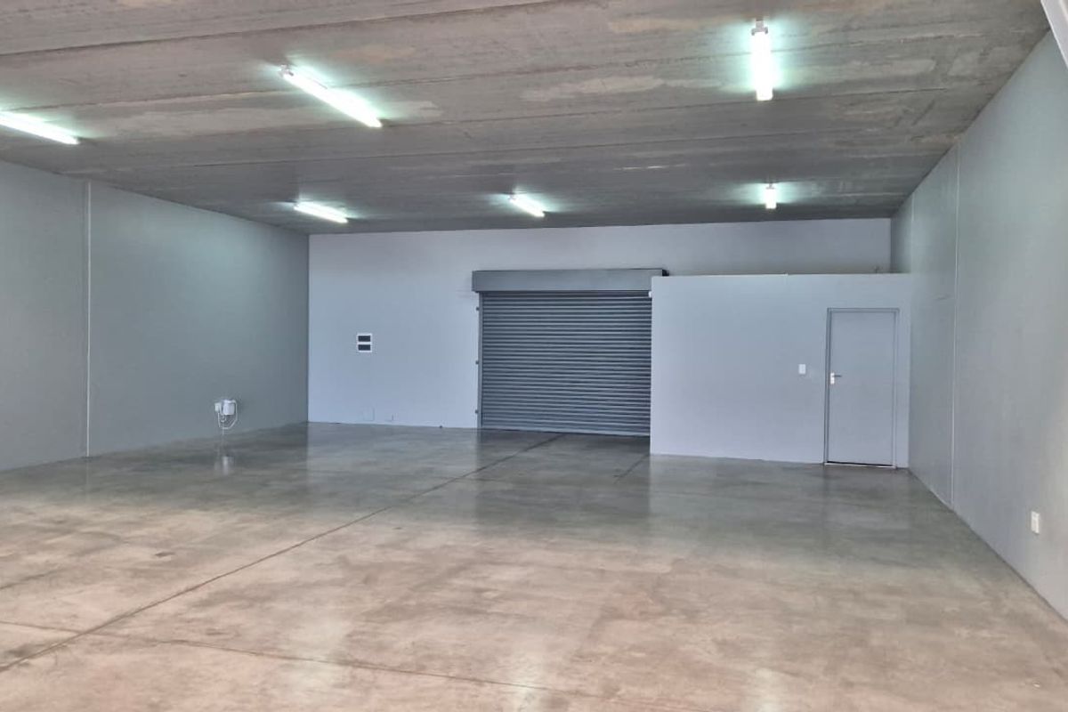 A spacious, open-plan utility or warehouse space featuring polished concrete flooring, a high concrete ceiling, and a secure roller shutter door.