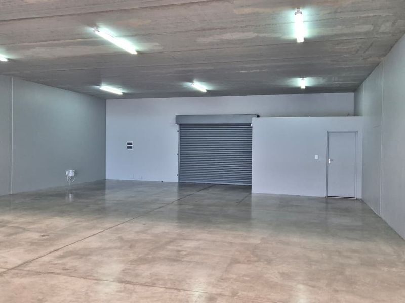A spacious, open-plan utility or warehouse space featuring polished concrete flooring, a high concrete ceiling, and a secure roller shutter door.