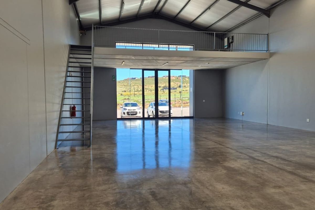 Spacious open-plan retail or industrial unit featuring polished concrete floors, a mezzanine level with metal staircase, and high ceilings with exposed steel trusses.